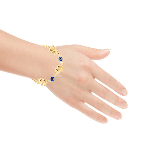 A hand adorned with a Blue Evil Eye and Elephant Charms Bracelet rests against a white background. This captivating piece of 14k gold-filled jewelry showcases alternating blue eye motifs and elephant charms, seamlessly merging cultural symbols into an eye-catching design.